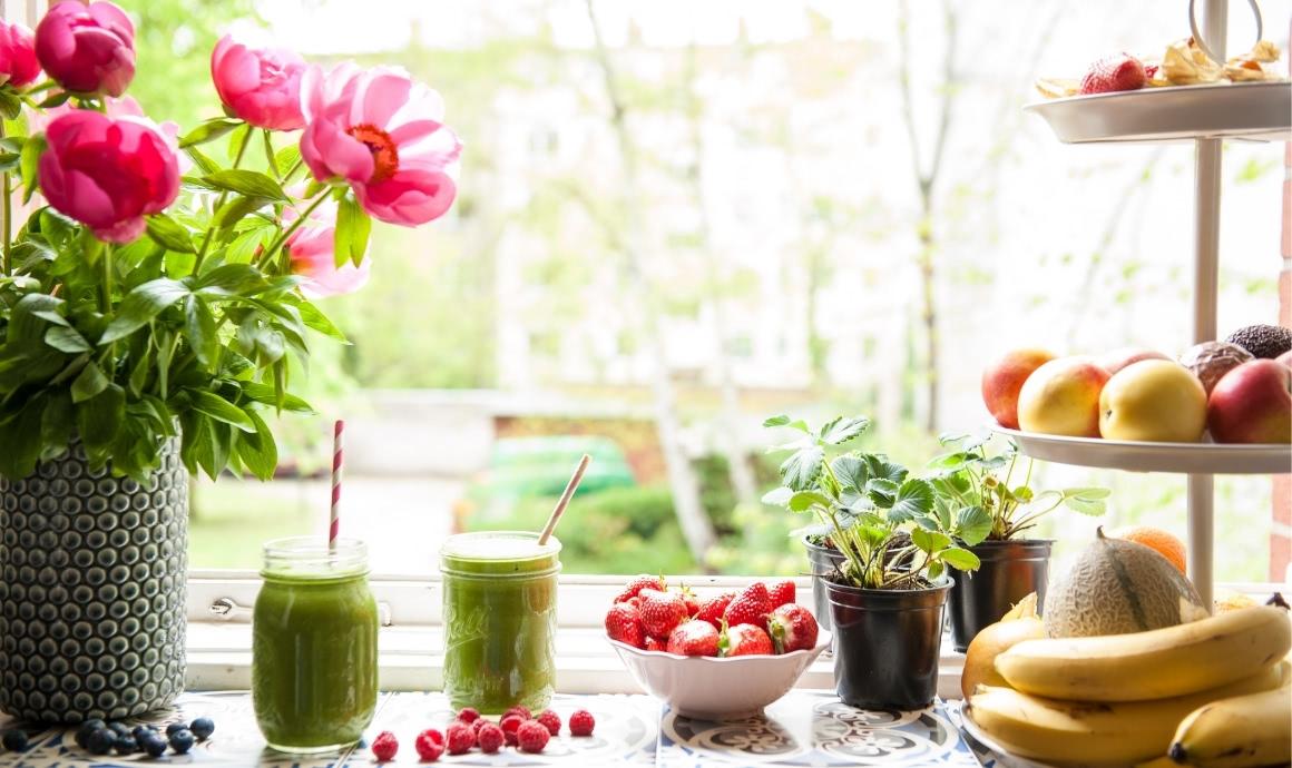 Green smoothies set-up on windowsill with lots of fruits and view