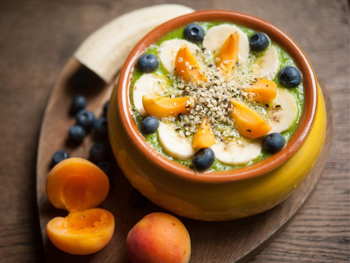 Green smoothie in a bowl with topping of peach, blueberries, bananas and hemp seeds