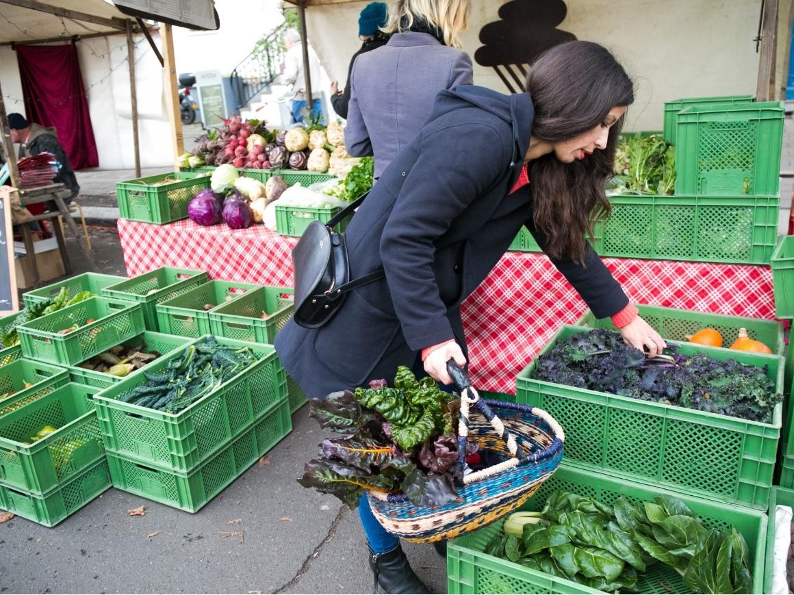 Woman selects fresh leafy greens at a weekly farmers' market stand.