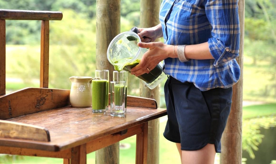 Woman pours green smoothies from container into glasses.