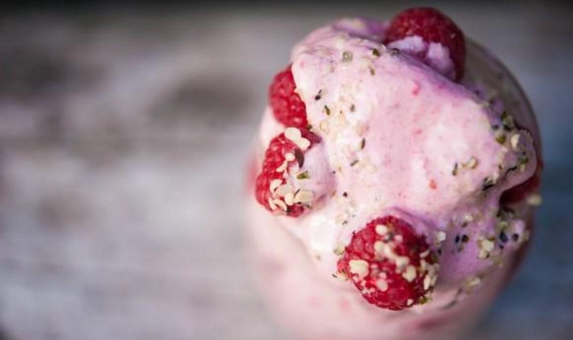 Pink nicecream in a glass with raspberries and hemp seeds as topping
